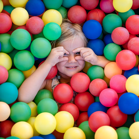 Una bambina spunta da una piscina di palline colorate.